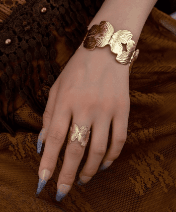 Woman wearing a large golden butterfly hand cuff and matching ring