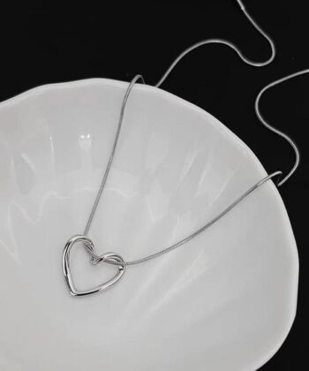 Close up of a silver Hollow Heart Pendant on a snake chain held in a hand