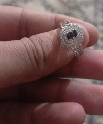 close-up view of a hand wearing a substantial silver-plated ring with a geometric cluster of three central black zircons and a surrounding halo of clear stones.