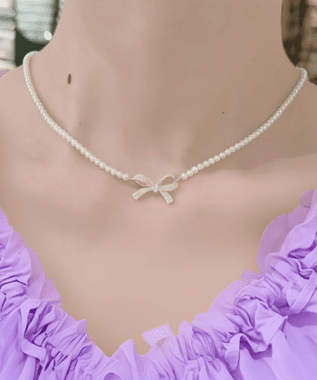 Woman wearing a white pearl choker with a sparkling crystal bow pendant