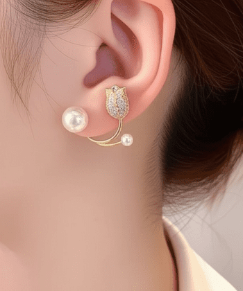 A close-up shot of a woman wearing a gold tulip ear jacket with zircon stones and pearls.