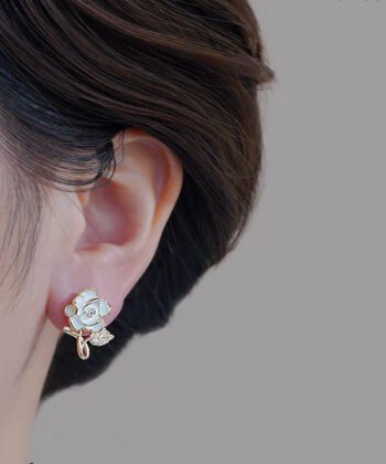 Close up of a woman wearing a white camellia flower stud earring with a golden crystal leaf