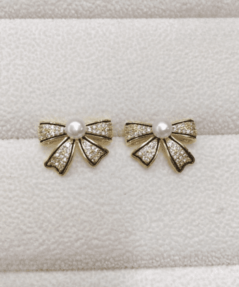 A pair of gold-toned bow-shaped earrings encrusted with small zircons and a white pearl in the center.