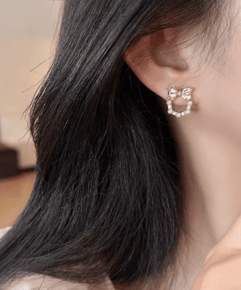 A close-up of a woman wearing a gold bow earring with a pearl wreath drop and zircon stones.