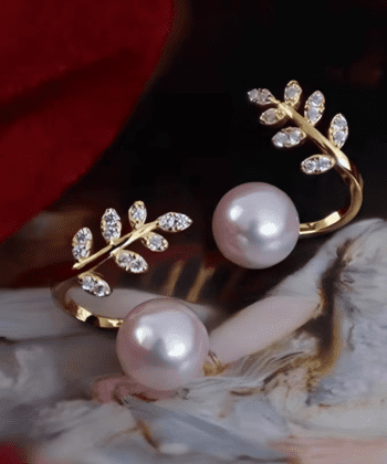 pair of golden earrings featuring a lustrous pearl next to a detailed leaf branch design