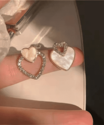 Close up of two different heart-shaped earrings with crystals and shell texture on a finger