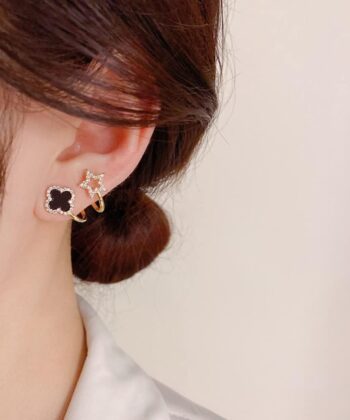 Elegant woman wearing gold ear cuffs with a black clover and a sparkling star design.
