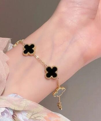 Gold chain bracelet with five black four-leaf clover charms on a white luxury background.