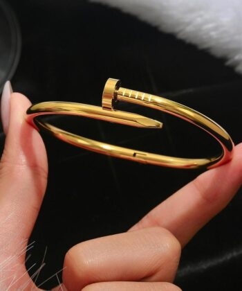 Premium gold nail-shaped bangle on a soft beige silk background.